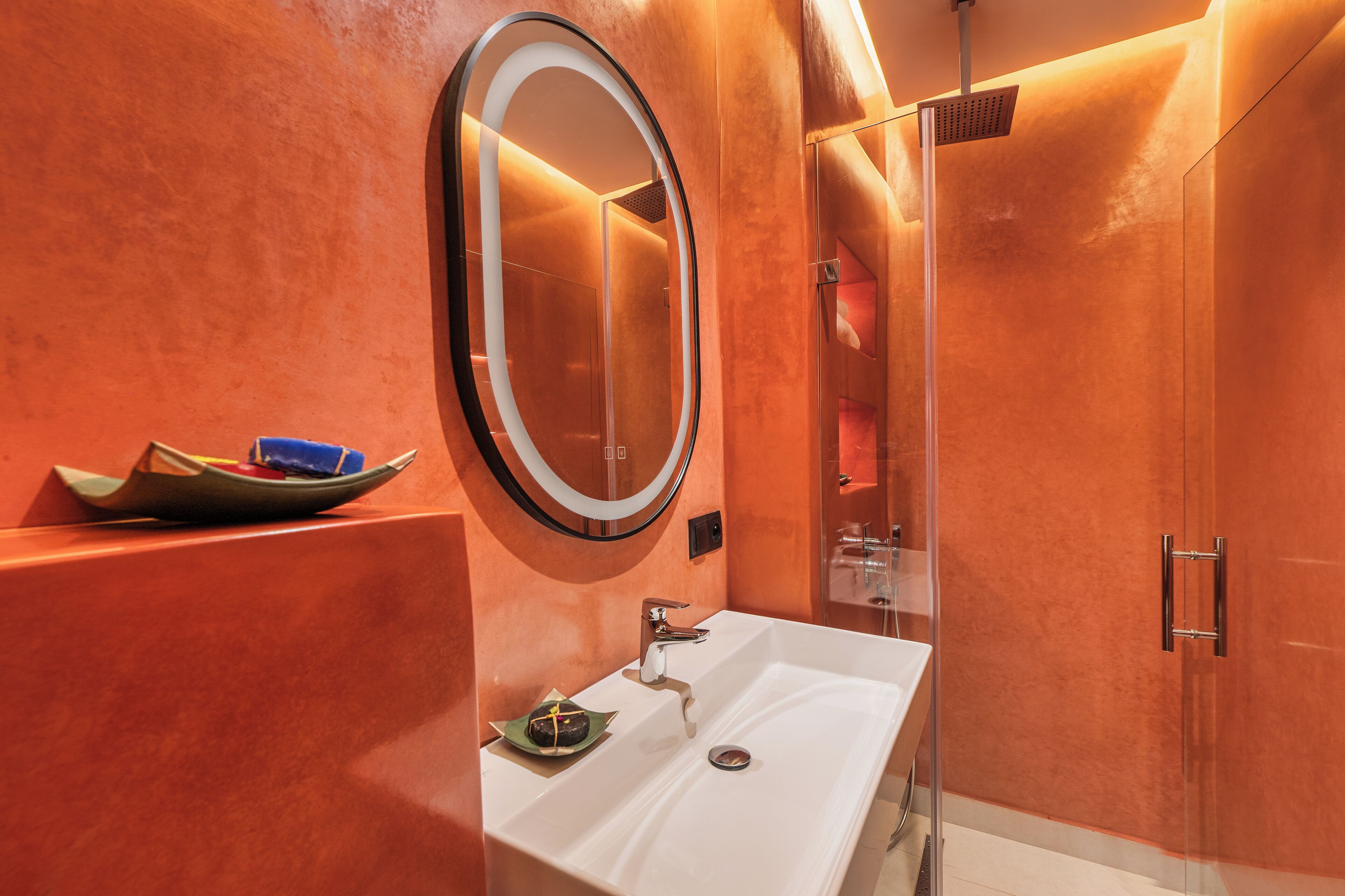 A modern bathroom with a large oval mirror, a white sink, and a glass-enclosed shower.