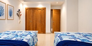 A bedroom with two beds, wooden wardrobe, and a door leading to another room. - Charming 2-bedroom apartment on the Beach! (Guayacanes)