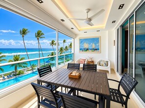 A balcony with a view of the ocean, a dining table with chairs, and a ceiling fan. - Charming 2-bedroom apartment on the Beach! (Guayacanes)