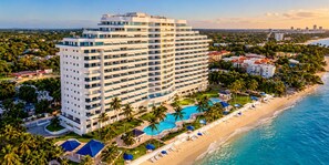 Een hoog hotel met meerdere balkons, een zwembad en een ligging aan het strand.