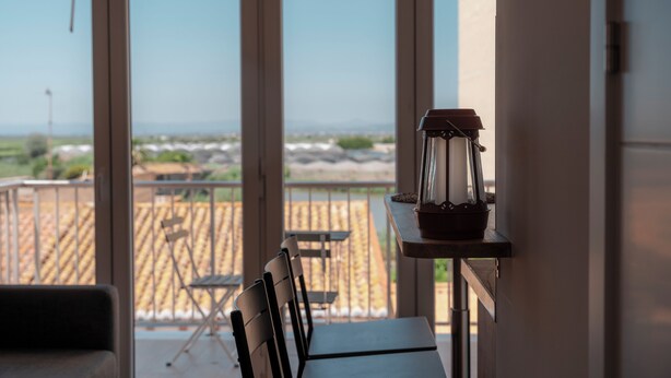 Un balcone con tavolo e sedie, una lanterna e vista sulla spiaggia e sull'oceano.