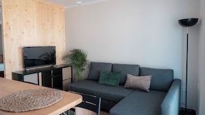 Un soggiorno moderno con un divano angolare grigio, un mobile TV in legno, una pianta in vaso e una lampada da terra.