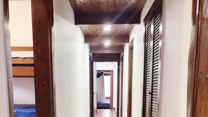 A narrow hallway with wooden floors and walls, leading to a room with a bed and a window with shutters. - Beach House Unid. 2 Casas Praia Guarujá (Guarujá)
