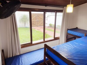 A dormitory room with two bunk beds, a large window with curtains, and a hanging fan. - Beach House Unid. 2 Casas Praia Guarujá (Guarujá)