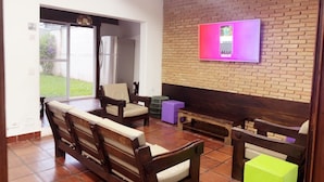 A living room with a brick wall, a television mounted on it, and a sliding glass door leading to a patio. - Beach House Unid. 2 Casas Praia Guarujá (Guarujá)