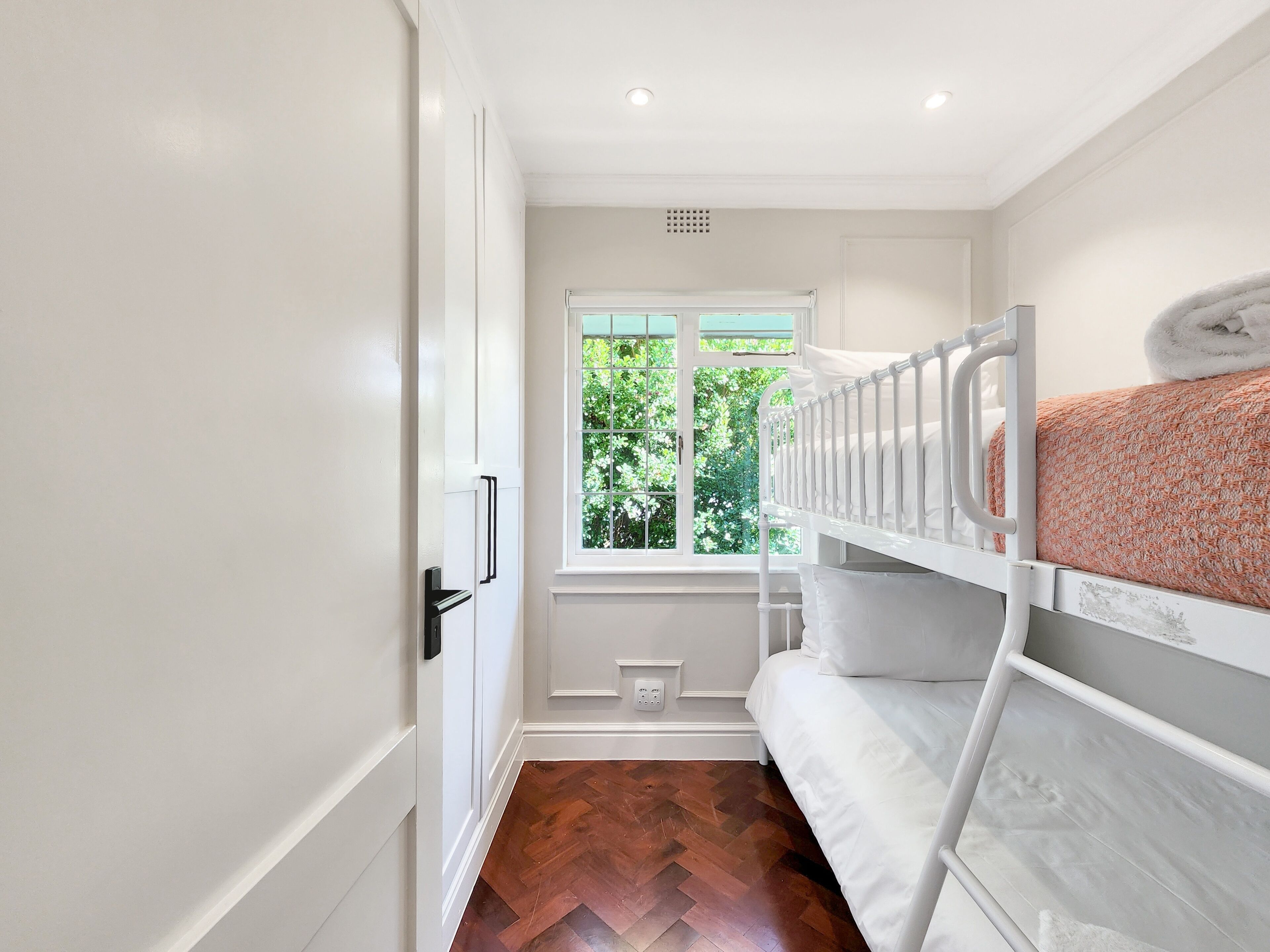A room with a bunk bed, a window with a view of greenery, and a door with a handle.