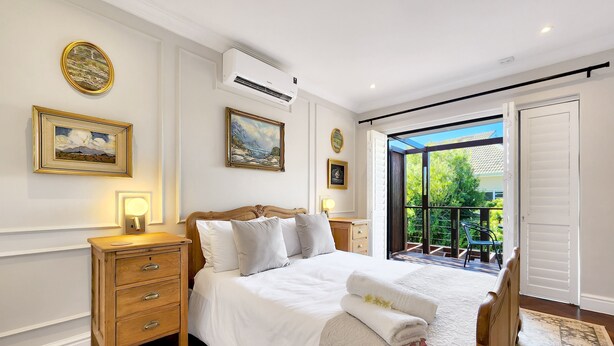 A well-appointed bedroom with a large bed, bedside tables, a nightstand, and a view of the outdoors. - Eagles Nest - Branch & Vine Cottages (Cape Town)