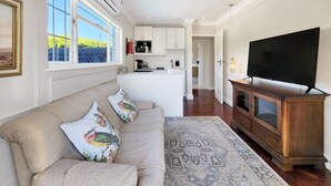 A modern living room with a beige sofa, colorful cushions, a patterned rug, a wooden cabinet, and a flat-screen TV. - Eagles Nest - Branch & Vine Cottages (Cape Town)