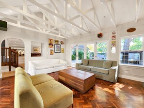 A spacious living room with a high ceiling, wooden flooring, and two sofas.