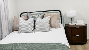A neatly arranged bedroom with a bed, pillows, a bedside table with a lamp, and a small drawer unit. - Cozy Private 1-Bedroom 1 Bathroom Suite  (Calgary)