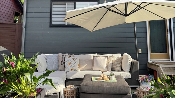 A patio with a gray sofa, a beige umbrella, and string lights against a gray house. - Cozy Private 1-Bedroom 1 Bathroom Suite  (Calgary)