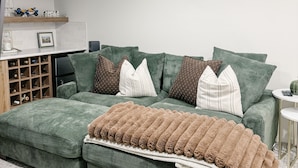 A modern living room with a green sofa set, a wooden shelf with decorative items, and a marble floor. - Cozy Private 1-Bedroom 1 Bathroom Suite  (Calgary)