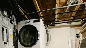 A laundry room with stacked washers and dryers, electrical panels, and exposed wooden beams. - Cozy Private 1-Bedroom 1 Bathroom Suite  (Calgary)