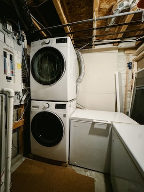 Une buanderie équipée d’une machine à laver et d’un sèche-linge superposés, de panneaux électriques et de poutres en bois apparentes.