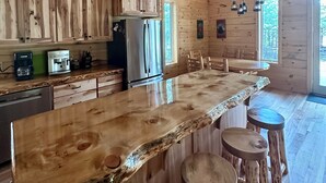 A rustic wooden cabin kitchen with a large island, bar stools, and a refrigerator. - Pine Cabin on Gilmore Lake (Minong)