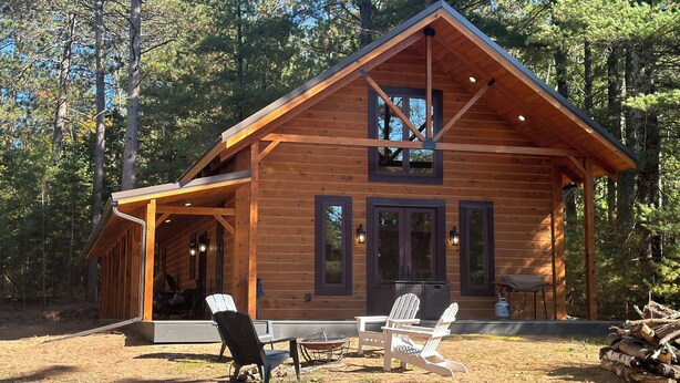 A wooden cabin with a porch, two Adirondack chairs, and a fire pit. - Pine Cabin on Gilmore Lake (Minong)