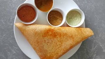 A triangular dosa with four small bowls of chutney on a white plate.