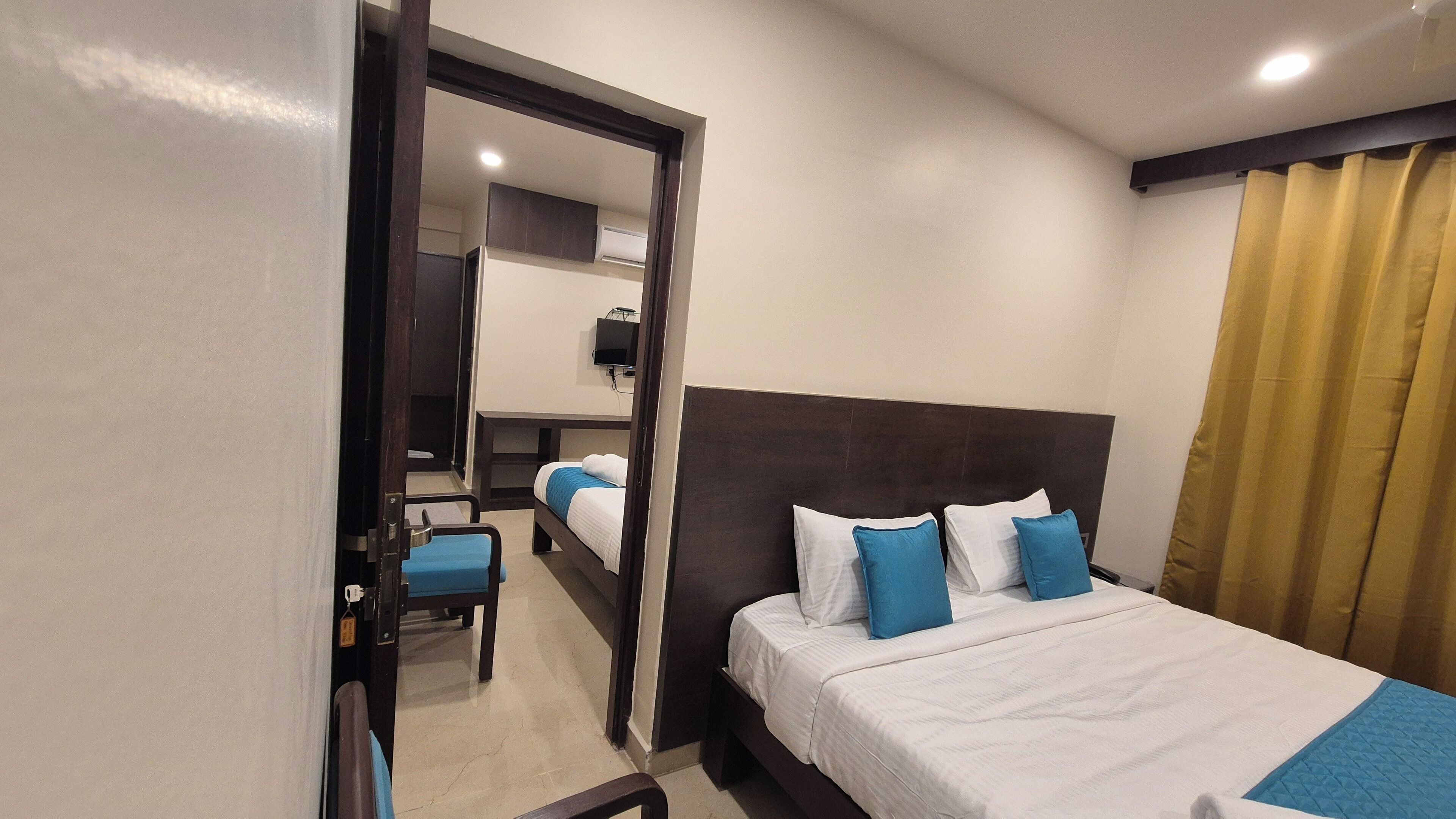 A hotel room with a bed, a desk, and a chair. There is a mirror on the wall and a window with curtains.