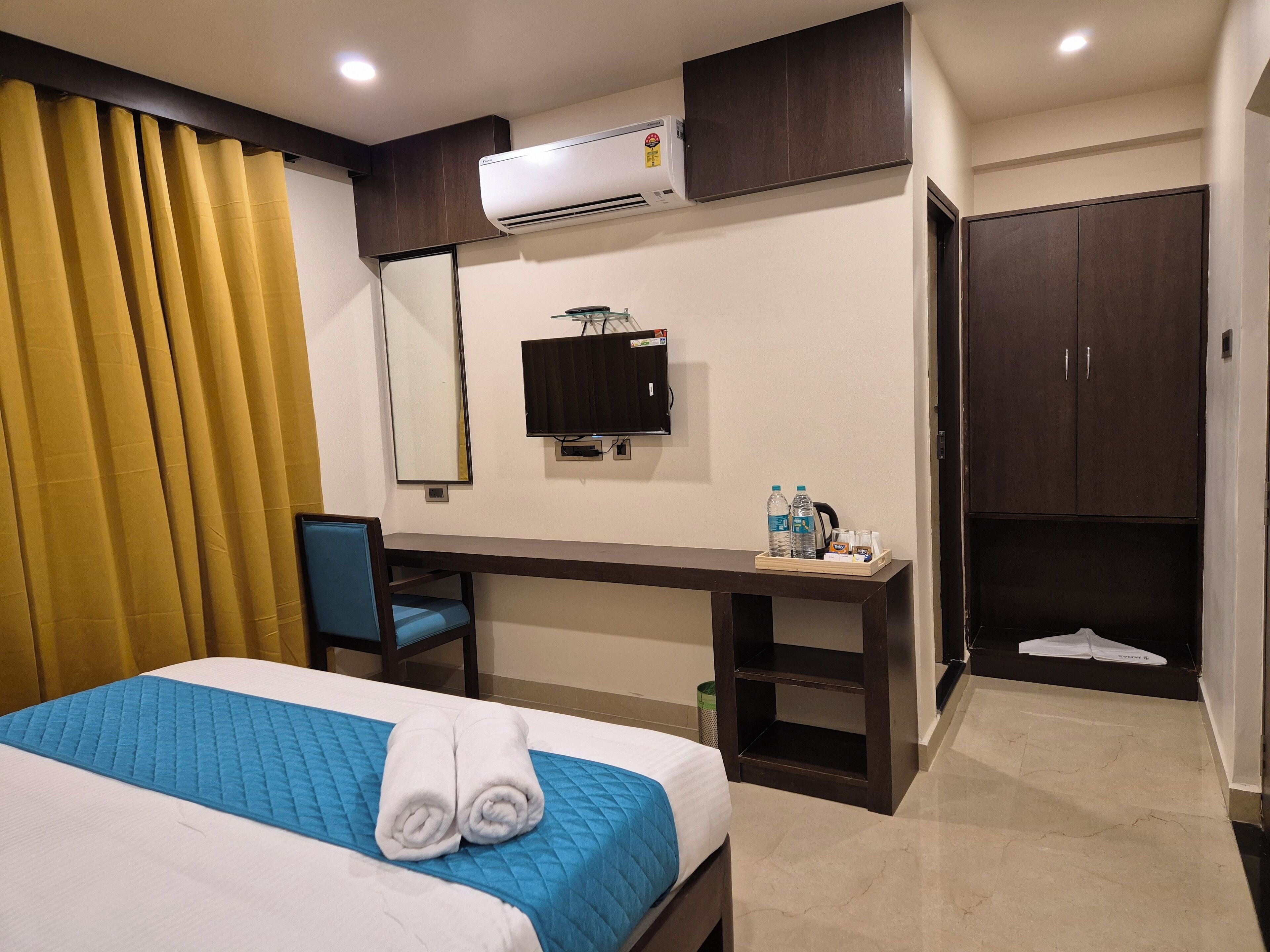 A hotel room with a bed, a desk, a chair, an air conditioner, a television, and a wardrobe.