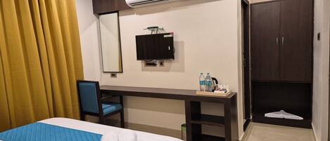 A hotel room with a bed, a desk, a chair, an air conditioner, a television, and a wardrobe.