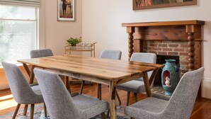A dining room with a wooden table, grey upholstered chairs, a patterned rug, a fireplace, and two framed artworks. - Lavender Hill Bed & Breakfast (Athens)