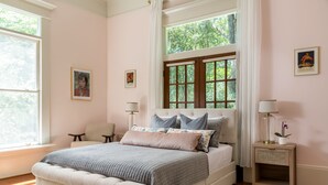 A bedroom with a large bed, a nightstand, a chair, and a window with curtains. - Lavender Hill Bed & Breakfast (Athens)