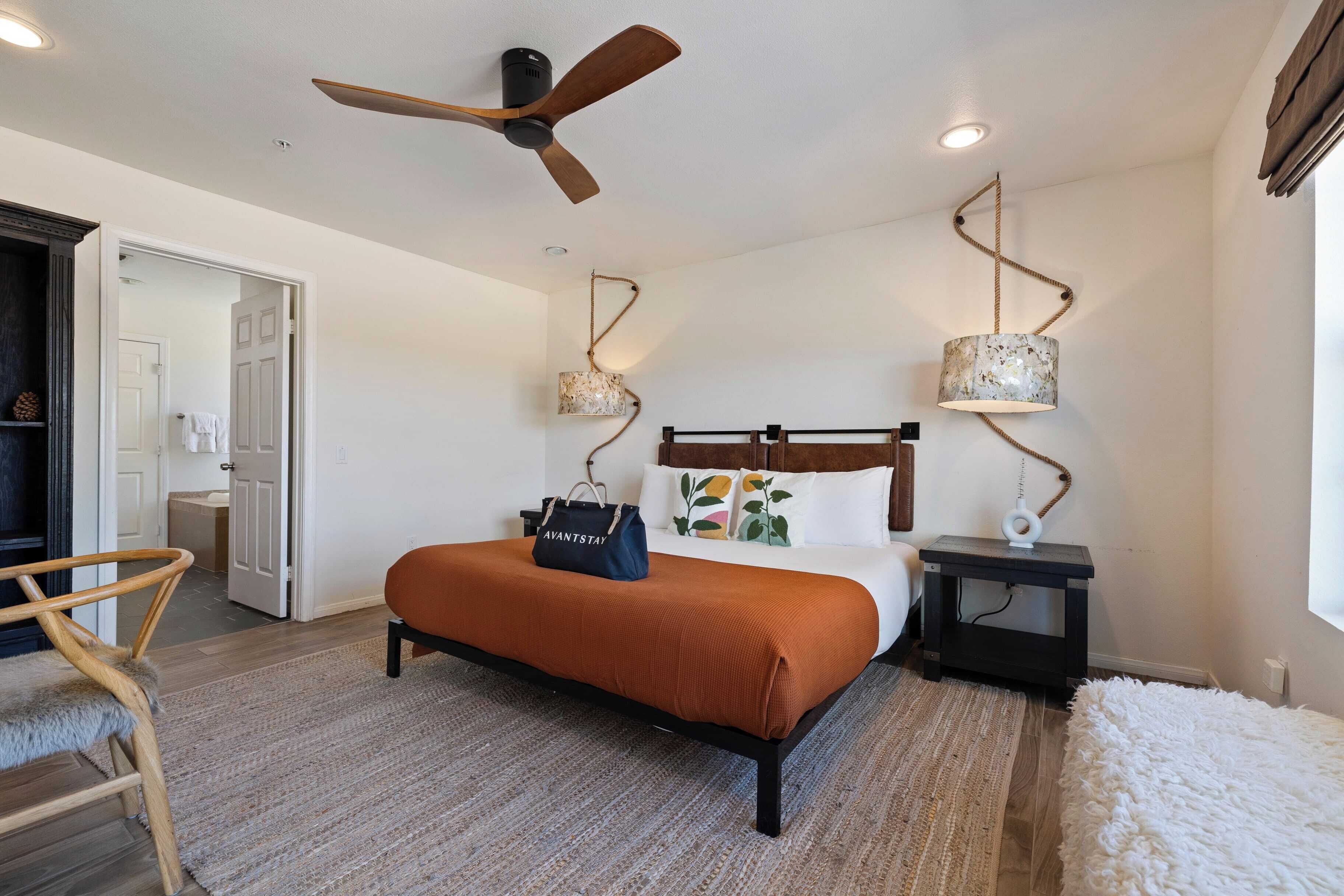 A bedroom with a bed, a nightstand, a chair, a ceiling fan, and a window.