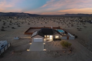 A modern house with a swimming pool, surrounded by a desert landscape with mountains in the background.