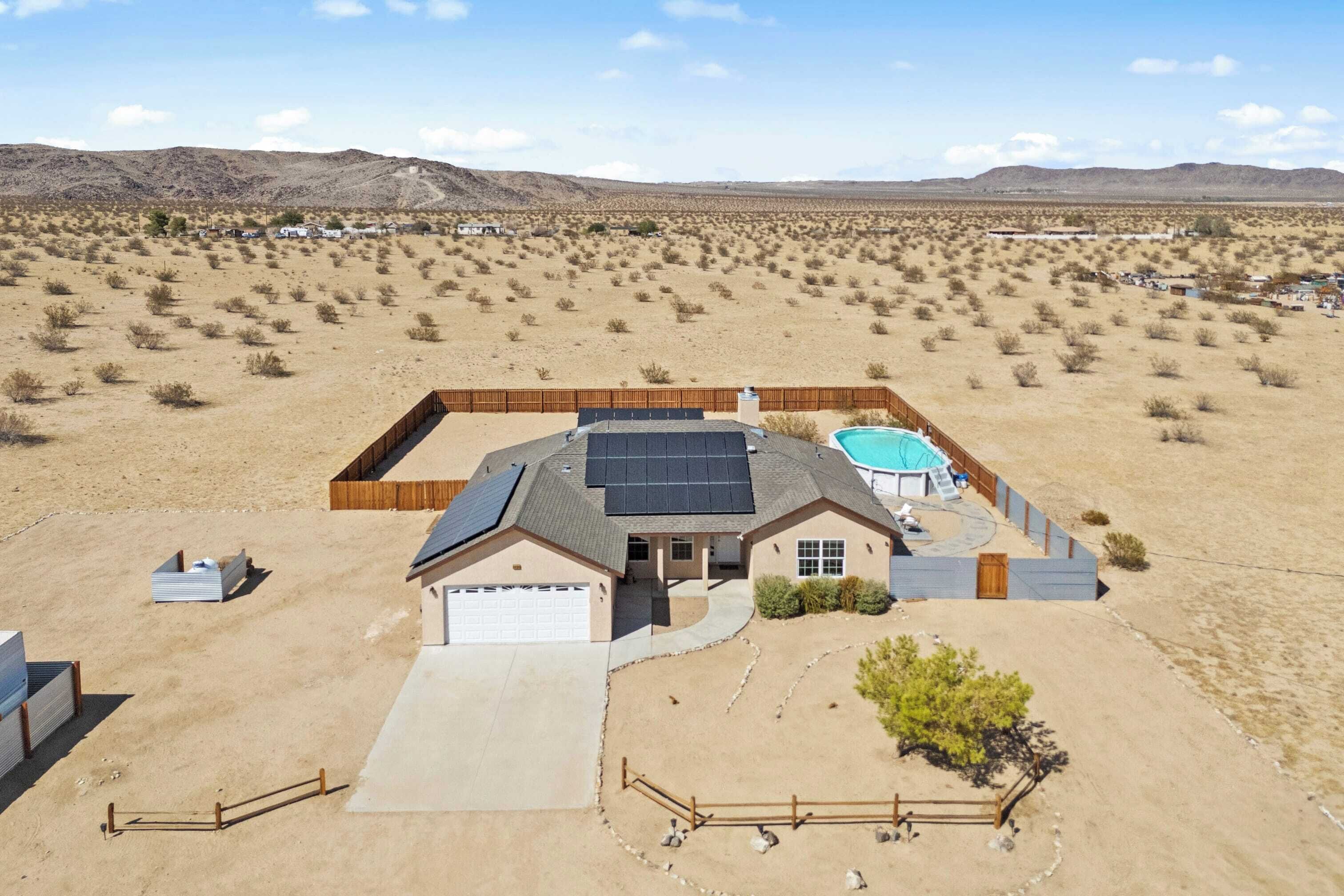 A house with a garage, solar panels, a swimming pool, and a desert landscape in the background.