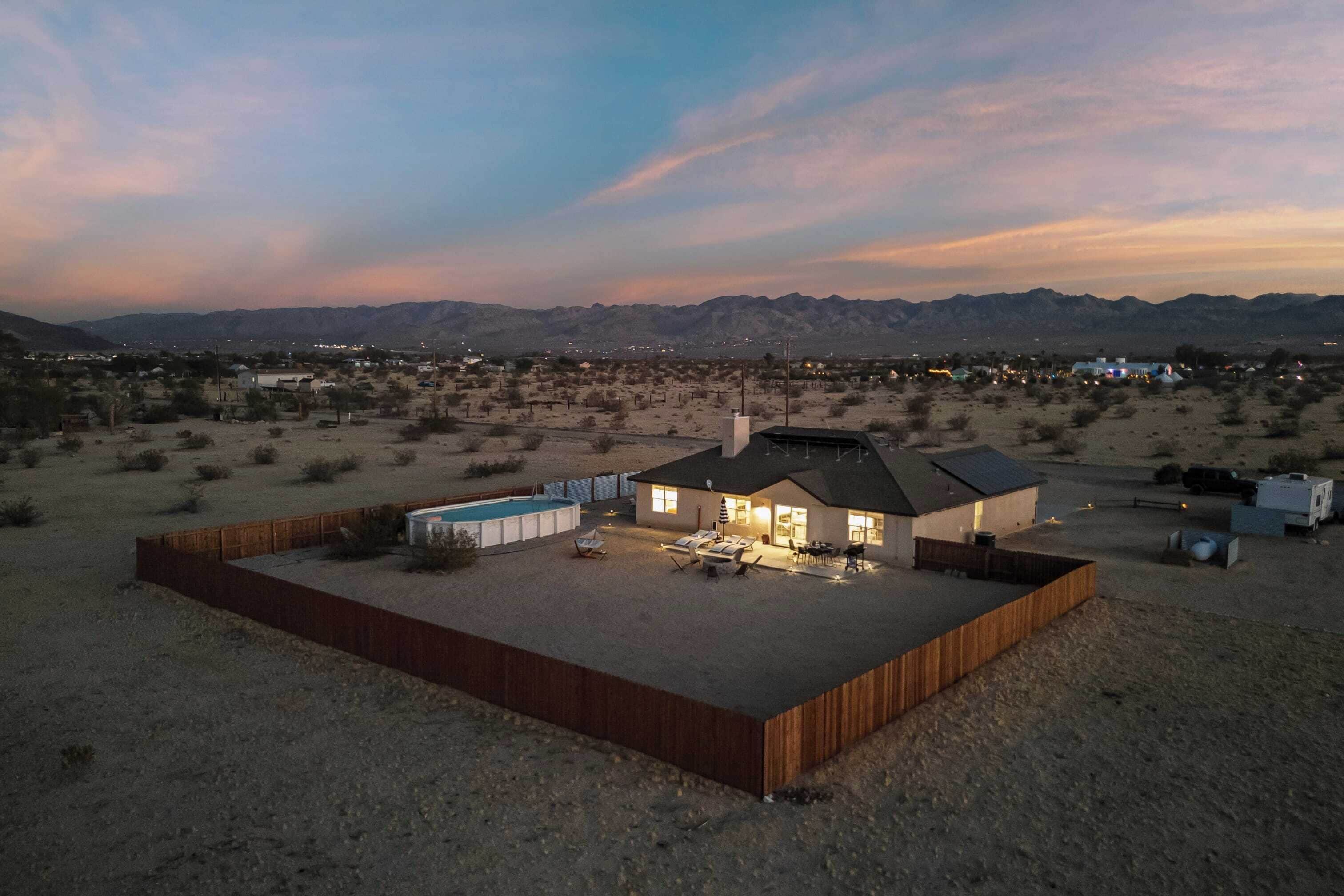 Une maison moderne avec un jardin clôturé, une piscine et une vue sur les montagnes.