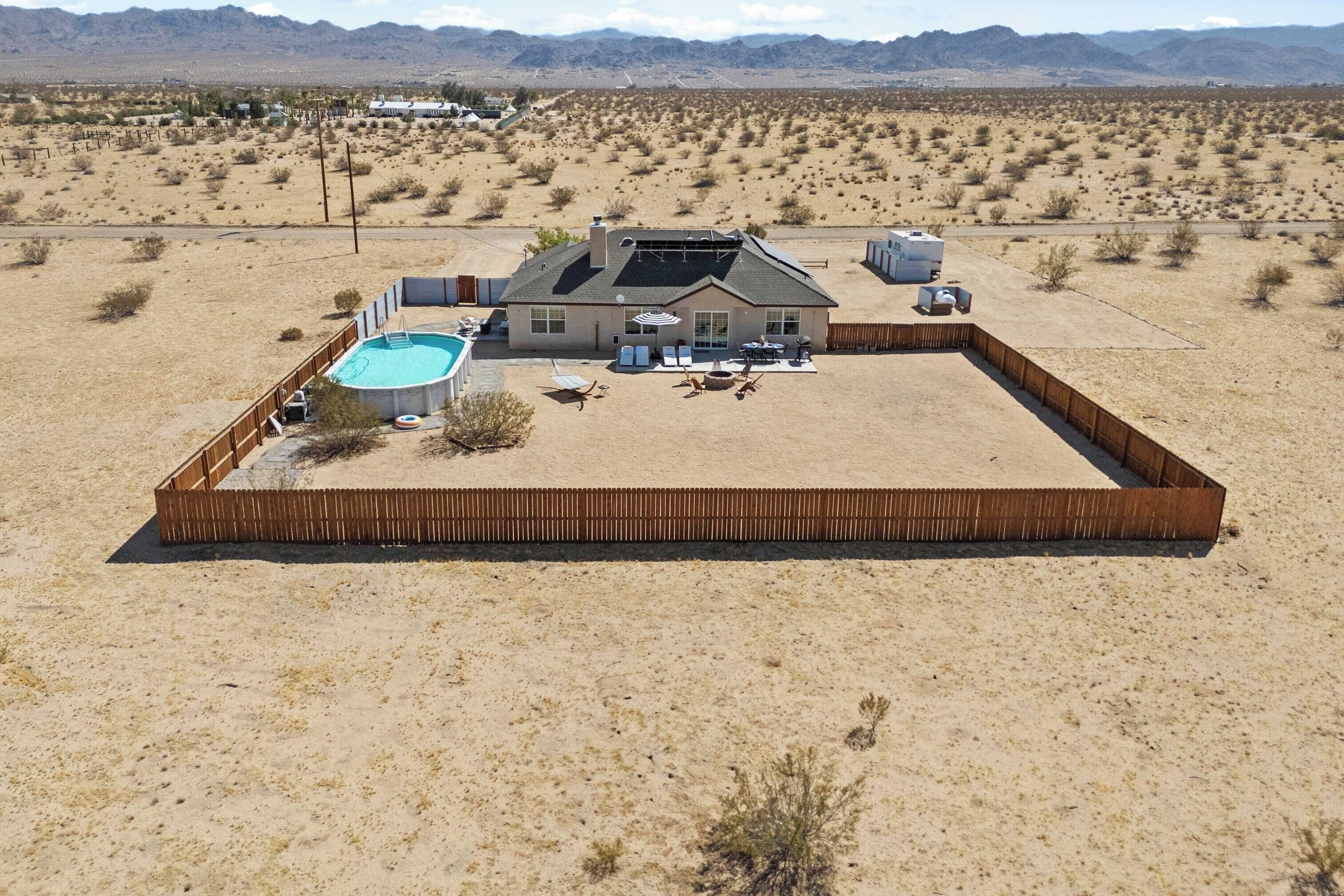 A house with a swimming pool, surrounded by a fenced yard, in a desert landscape.