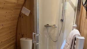 Un baño rústico en una cabaña de madera, con un inodoro, ducha y lavabo.