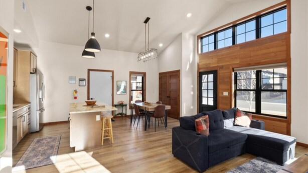 A spacious living area with a dark-colored sofa, a wooden dining table, and a kitchen area with a refrigerator and a stove.