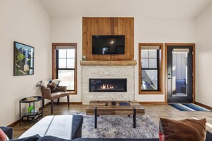 A spacious living room with a fireplace, a comfortable seating area, and a large TV mounted above the fireplace. - 13 Alpine Basin Loop (Red Lodge)
