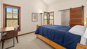 Un dormitorio con cama, escritorio y silla. Hay dos ventanas y una puerta.