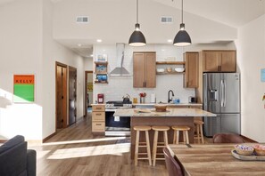 A modern kitchen with wooden cabinets, a stainless steel refrigerator, and a central island with stools. - 13 Alpine Basin Loop (Red Lodge)