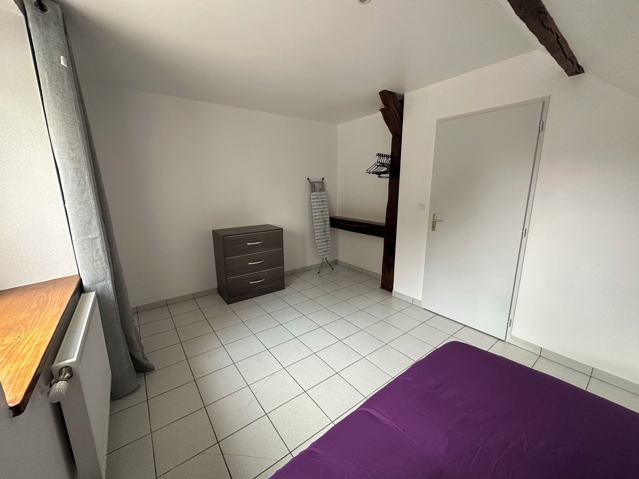 Een slaapkamer met een bed, een dressoir, een radiator en een deur.