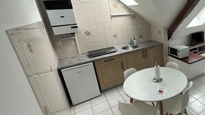 Uma cozinha moderna com área de refeições, apresentando piso de azulejos brancos, uma geladeira compacta, micro-ondas e uma mesa de jantar com cadeiras.