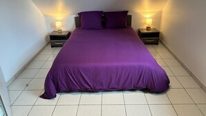 Quarto com uma cama grande, duas mesas de cabeceira com abajures e piso de azulejos.