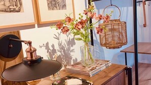 Un escritorio de madera con una lámpara, un florero con flores, una cesta y una estantería con perchas.