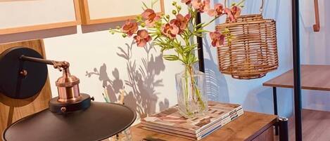 A wooden desk with a lamp, a vase with flowers, a basket, and a shelf with hangers.