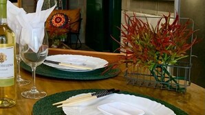 Una mesa de comedor servida con platos, cubiertos y una botella de vino, con una planta decorativa y una obra de arte enmarcada al fondo.