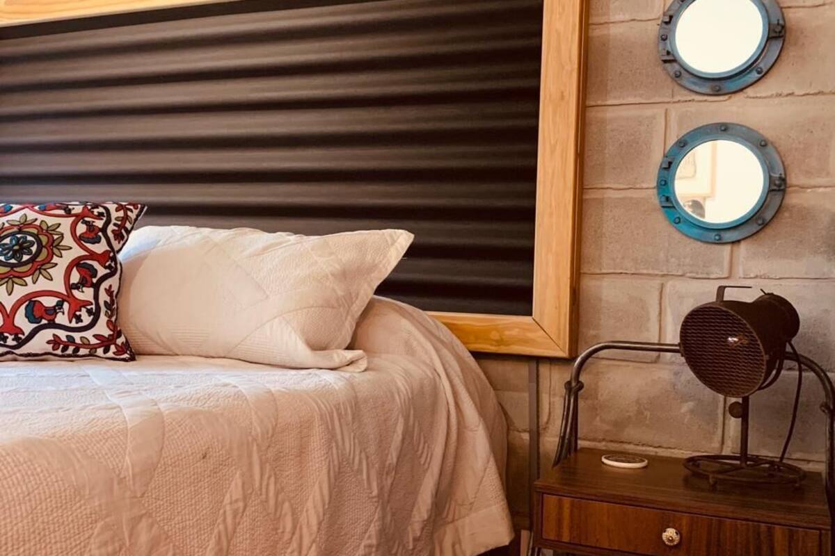Een bed met hoofdeinde, twee kussens, een nachtkastje met lamp en twee spiegels aan de muur.