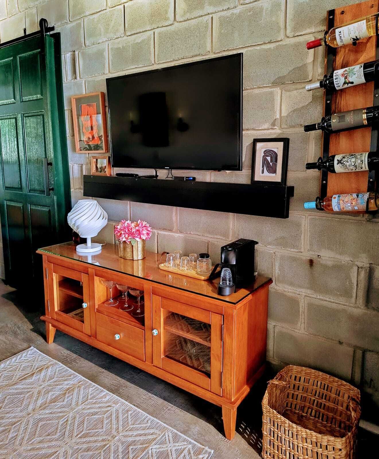 A living room with a TV mounted on a brick wall, a wooden cabinet with glass doors, and a wine rack on the wall.