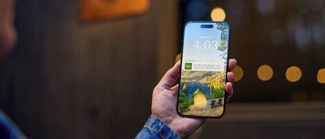 Una persona sosteniendo un teléfono inteligente que muestra un mensaje sobre una escapada a la naturaleza y la vista de una cabaña.