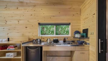 A compact kitchen with wooden walls, a window, a sink, a stove, and a dishwasher.