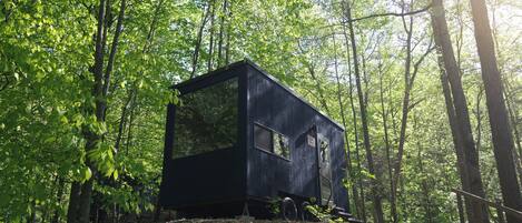 Una cabaña moderna de color oscuro en un área boscosa, con una escalera de madera que lleva hacia ella.
