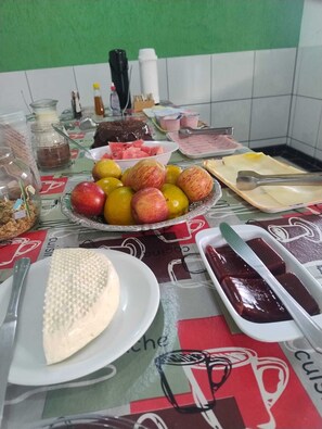 A table with various food items including fruits, a cake, and condiments. - POUSADA SÃO JUDAS TADEU (Guaratingueta)