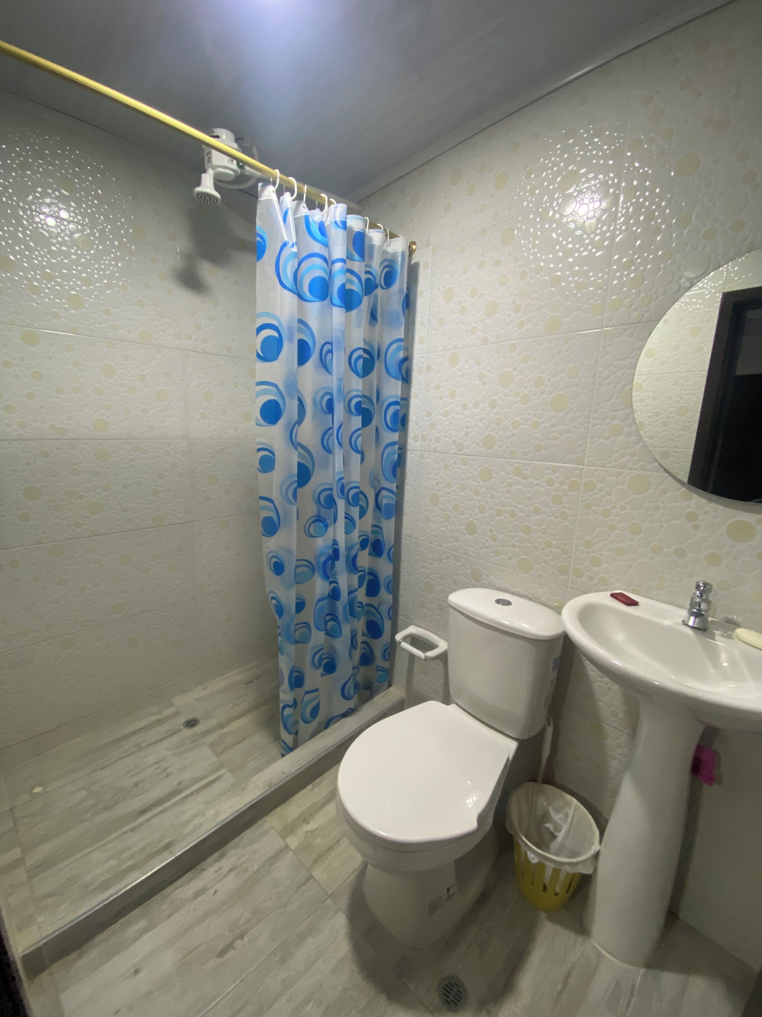 A bathroom with a toilet, bidet, sink, and a shower curtain with a blue pattern.
