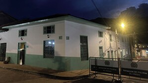 Comisaría con fachada blanca y detalles verdes, con ventanas protegidas por barrotes y un portón metálico al frente.